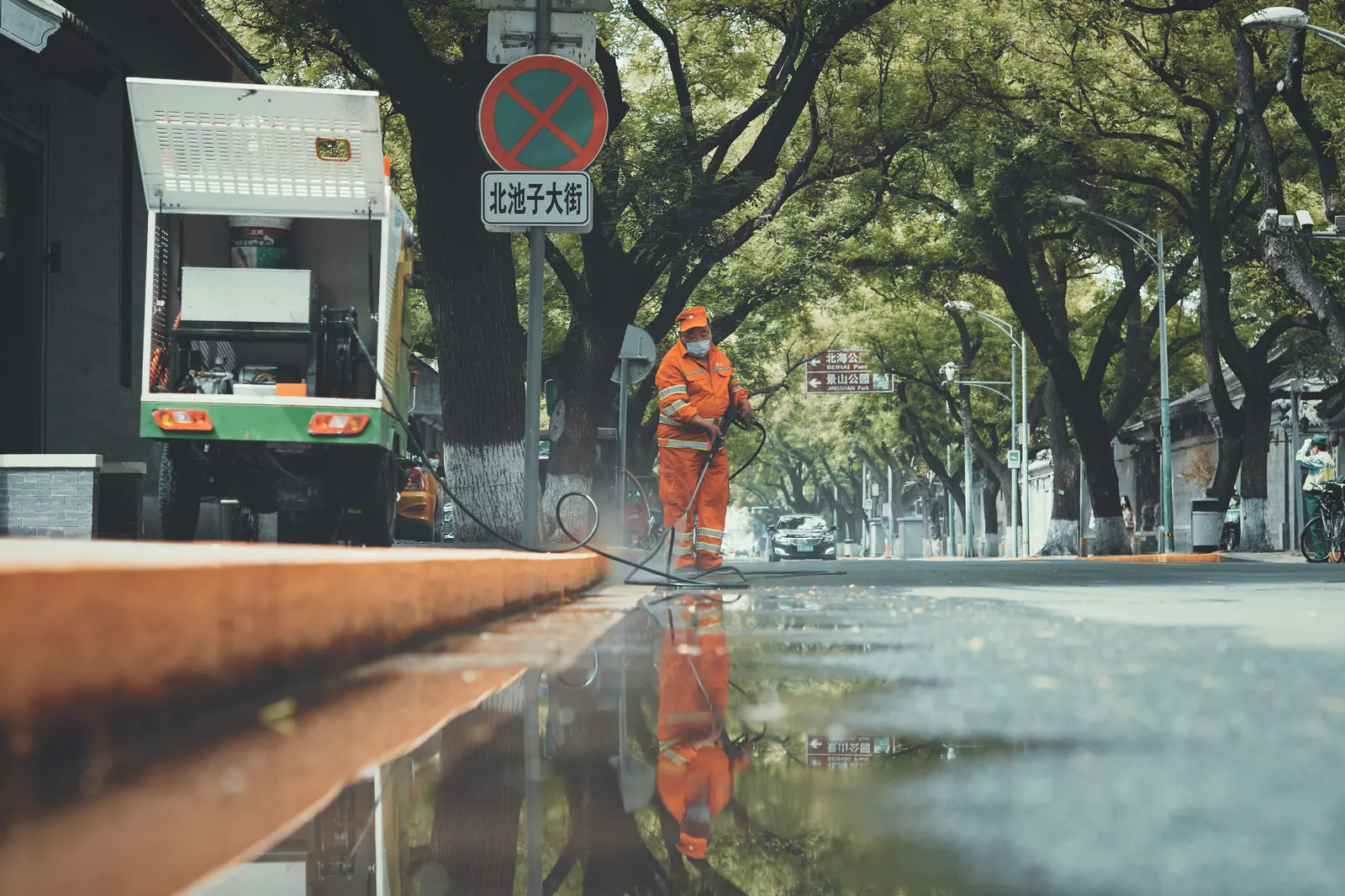 A Beijing street reflected in rainwater beside a passing bus