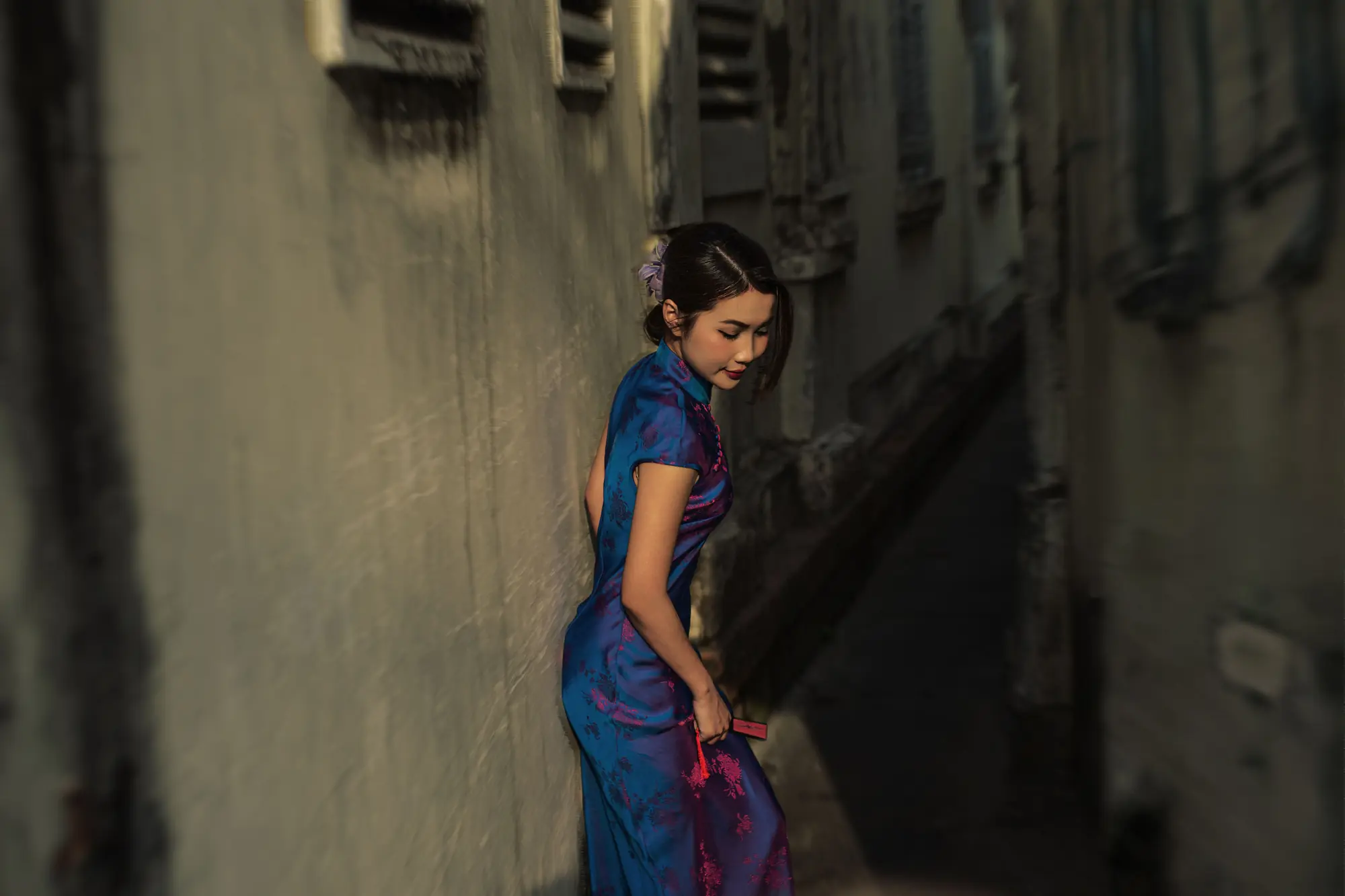 A woman in a blue qipao standing in a narrow Shanghai lane