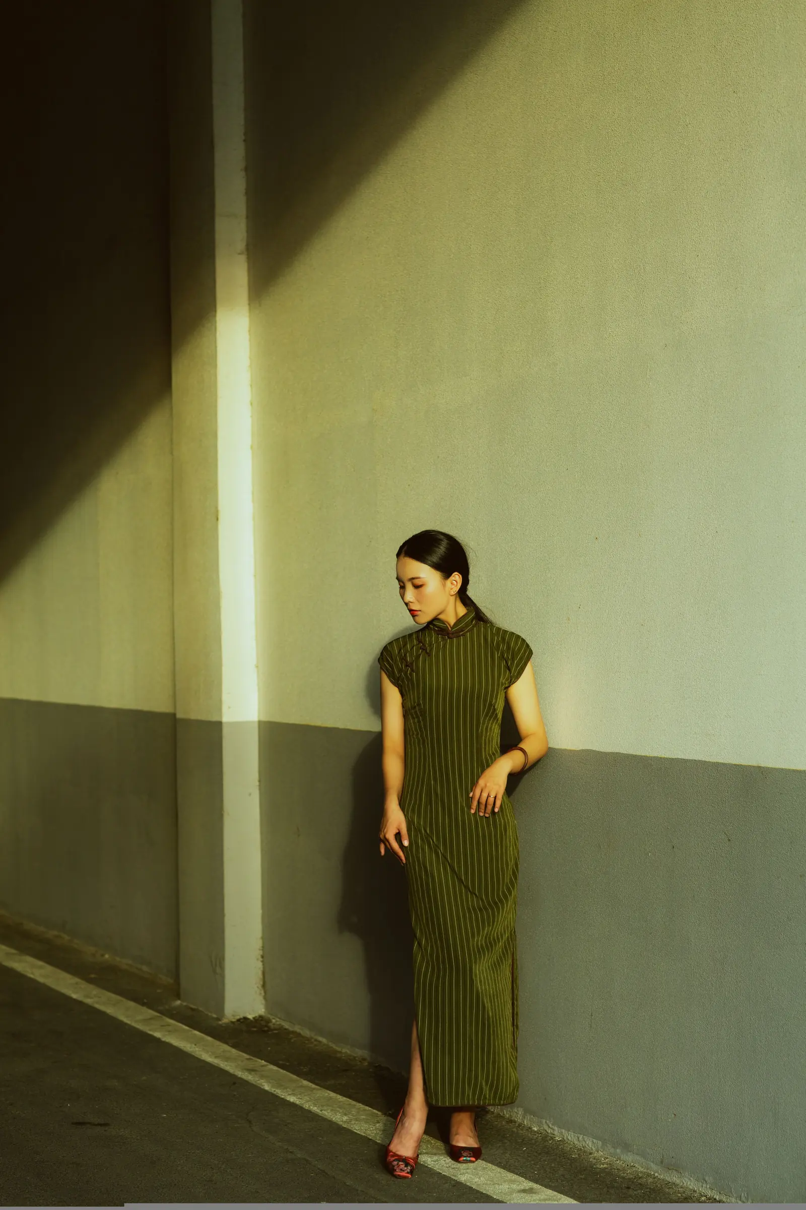 A woman in a dark qipao standing inside a shaft of golden light