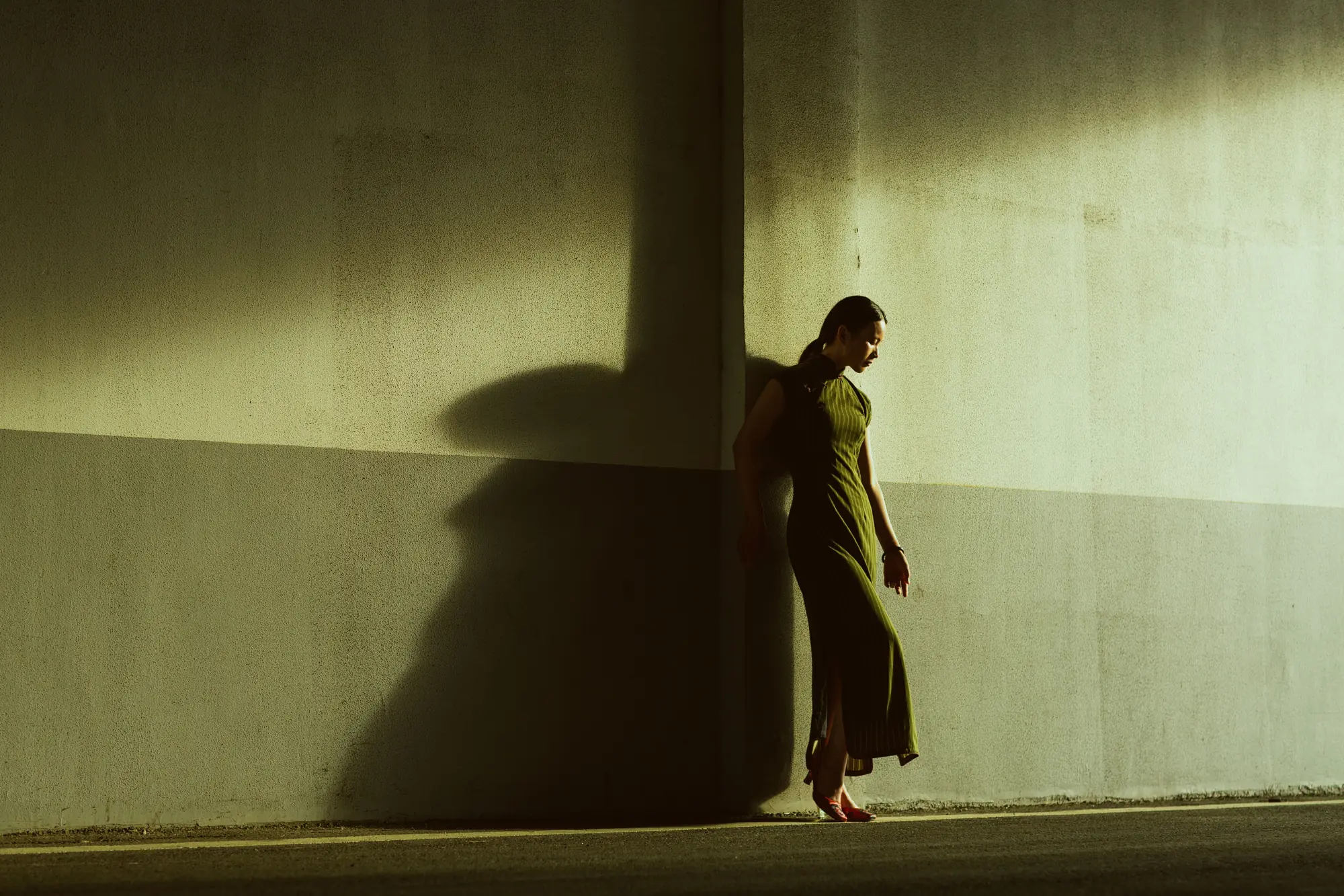 A woman in a dark qipao crossing a band of sunlight and shadow