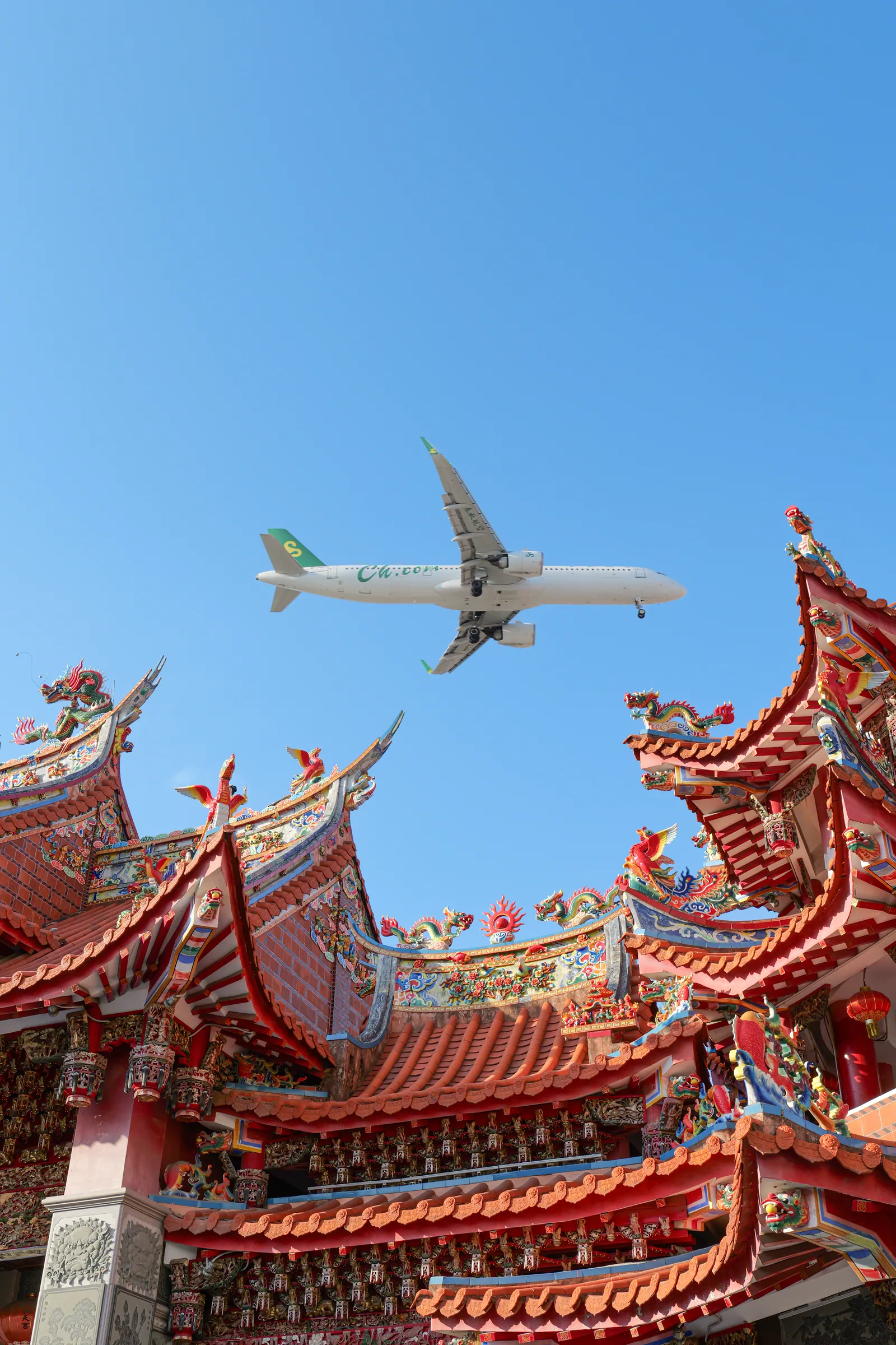 A Minnan temple roof beneath an aircraft crossing the blue sky