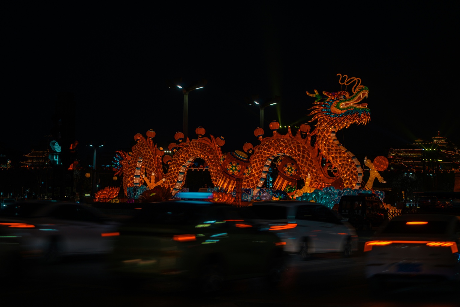 A large illuminated dragon lantern surrounded by moving traffic